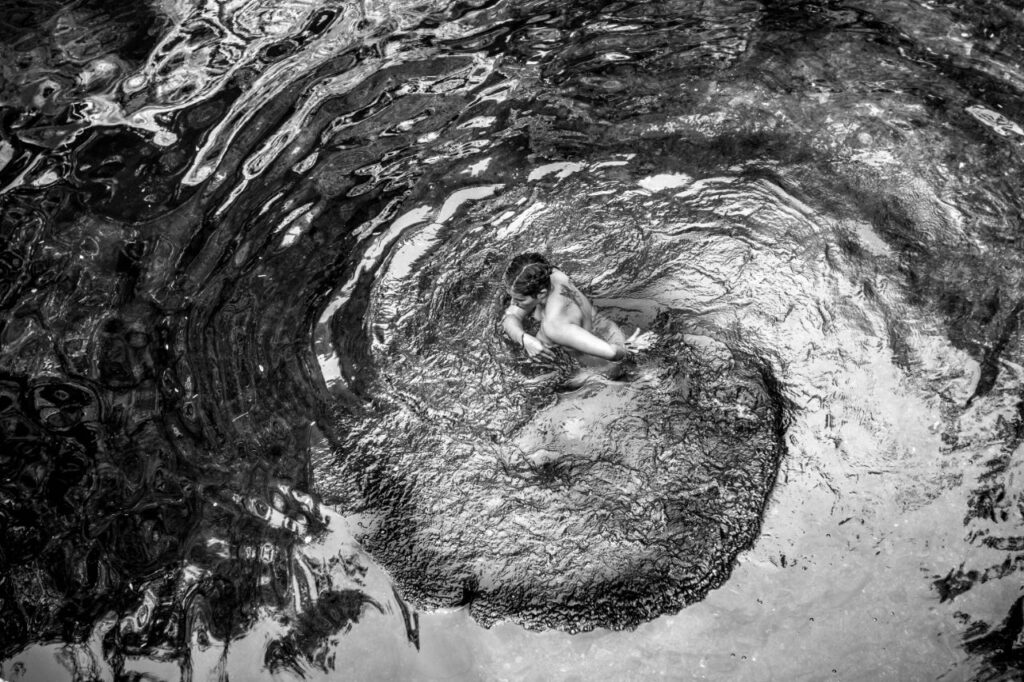 me veo bailando en el agua, generando un espiral alrededor de mi cuerpo. La foto es tomada desde arriba hacia el agua, en blanco y negro.
